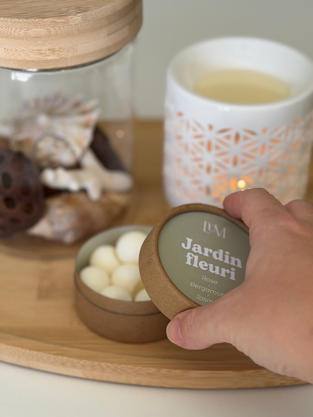 main qui ouvre une boite de fondants parfumés jardin fleuri avec brûle-parfum allumé en fond