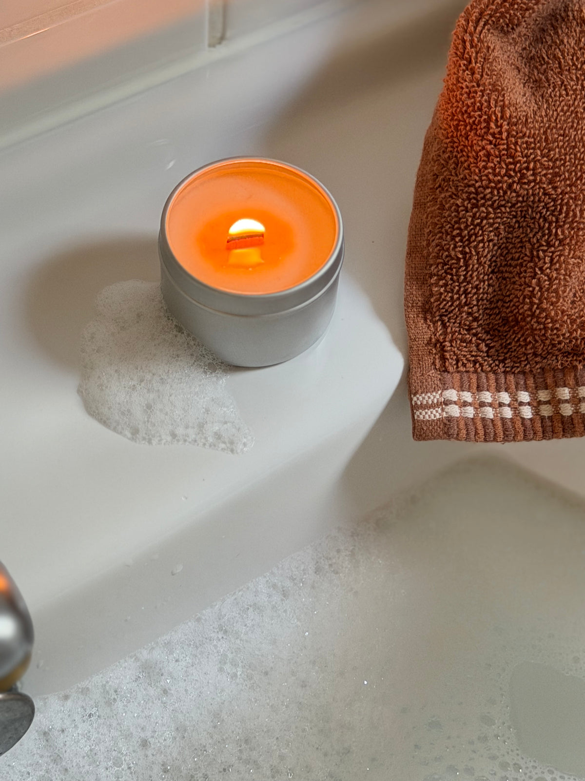 mini bougie LUM posée sur une baignoire avec mousse et serviette de bain