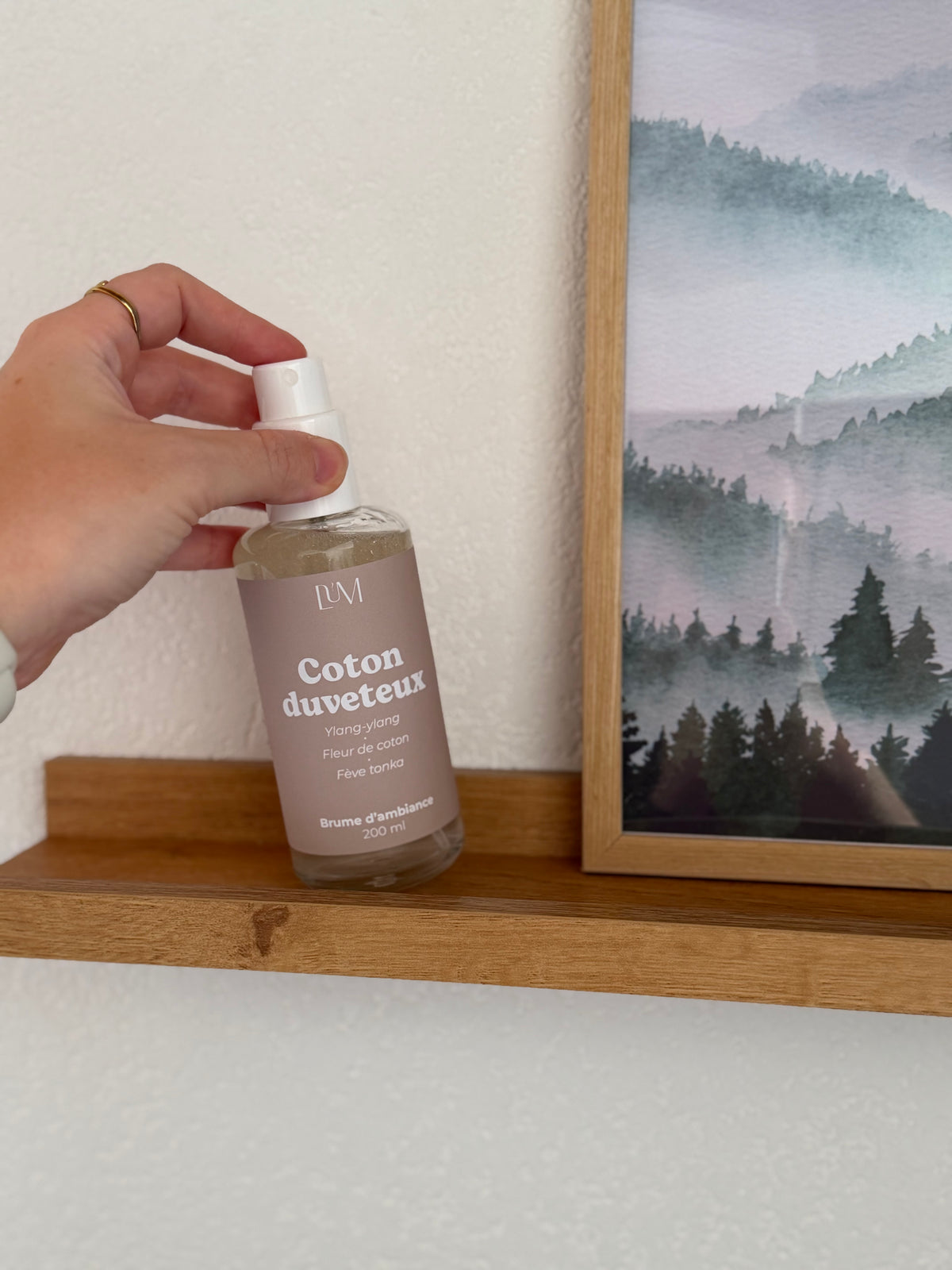 ambiance avec main qui pose une brume parfumée flacon verre transparent sur une étagère 