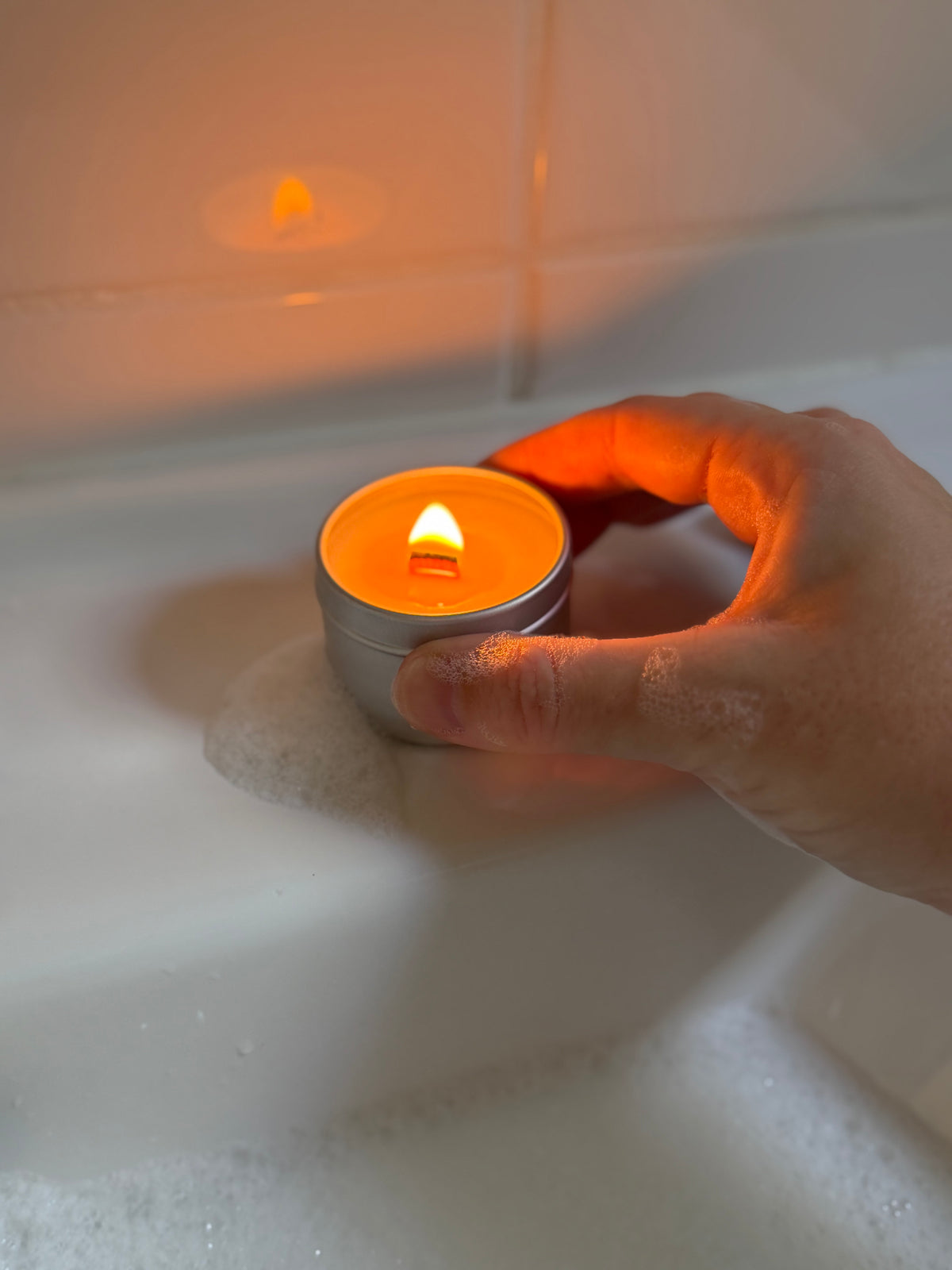 main savonneuse tient mini bougie LUM allumée sur le bord d'une baignoire